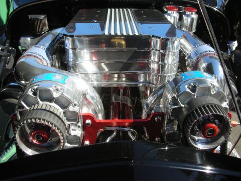 1998 Ford Crown Victoria - Front view of a polished dual-supercharger V8 engine with twin pulleys and a finned intake in a black hot rod.