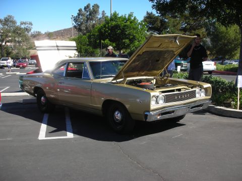1998 Ford Crown Victoria - gold late-1960s Dodge muscle car sits hood-up in a car-show lot with onlookers nearby.