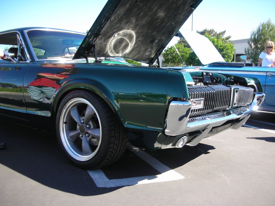 Front of dark green Mercury Cougar with hood up and gray five-spoke wheels