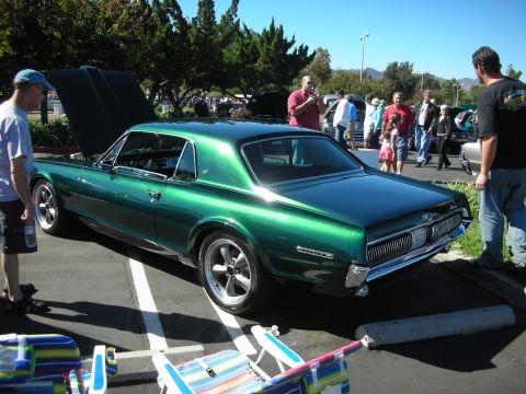 1998 Ford Crown Victoria - Rear three-quarter view of a dark-green Mercury Cougar hardtop coupe with hood up among car-show crowds.