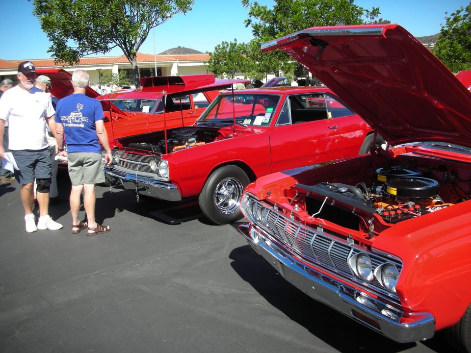Row of red muscle cars with hoods open at an outdoor car show