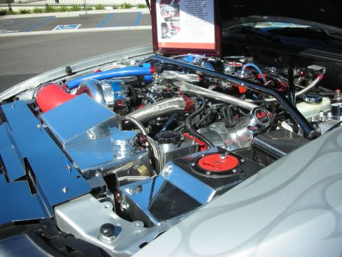 1998 Ford Crown Victoria - show-detailed engine bay full of braided stainless lines and red fittings, with a display card on the raised silver hood.