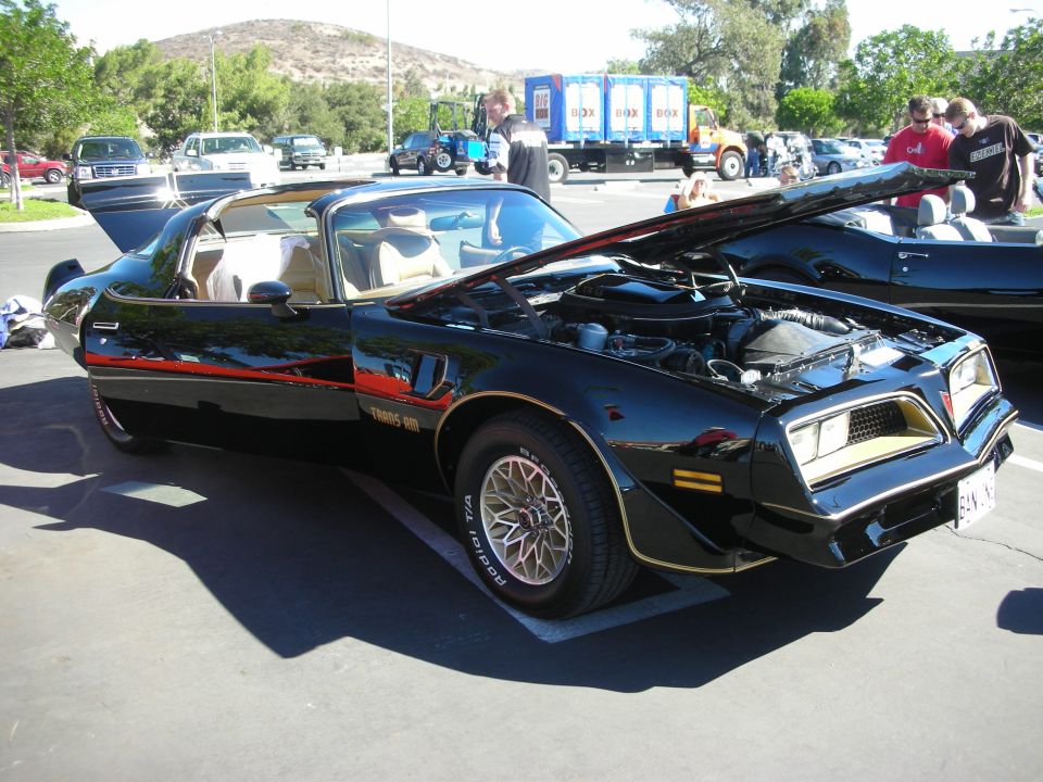 Black and gold Pontiac Trans Am with hood and T-tops open