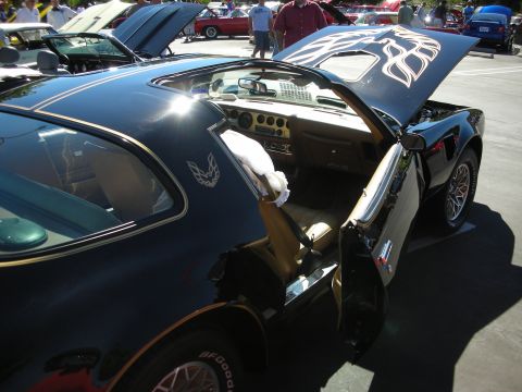 1998 Ford Crown Victoria - raised hood of a black Pontiac Trans Am reveals its gold firebird decal, with T-tops off exposing the interior.