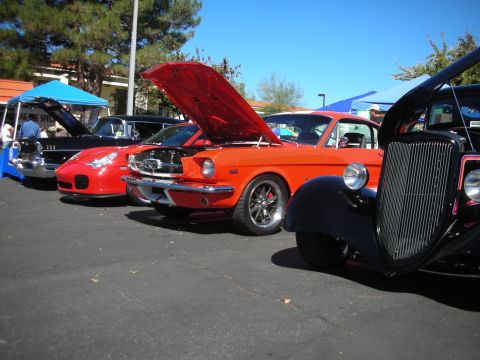 1998 Ford Crown Victoria - orange Ford Mustang fastback with hood up sits between a Porsche and a black hot rod at a car show.