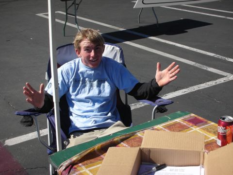 1998 Ford Crown Victoria - young man in a light blue shirt sits in a folding chair with hands raised, a Dr Pepper can on the table beside him.