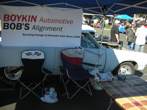 1998 Ford Crown Victoria - Boykin Automotive / Bob's Alignment banner hangs over a white car and folding chairs at a car-show booth.