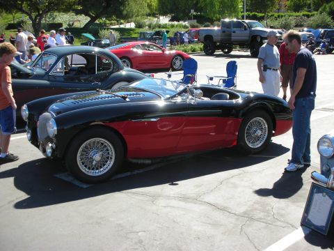 1998 Ford Crown Victoria - black-and-red vintage British-style roadster with chrome wire wheels draws onlookers at a sunny car show.