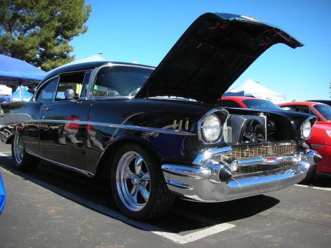 1998 Ford Crown Victoria - black 1957 Chevrolet Bel Air with chrome bumper and custom wheels sits with its hood raised at a car show.