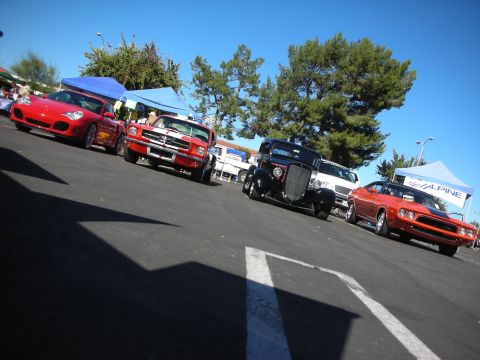 1998 Ford Crown Victoria - low-angle shot shows a red Porsche, Mustang, black hot rod and red Challenger lined up across a sunny show lot.