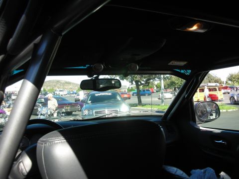 1998 Ford Crown Victoria - Looking out through a car's windshield past a roll bar and rearview mirror at classic cars at an outdoor show.