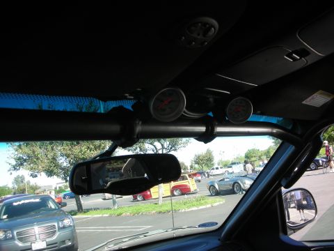 1998 Ford Crown Victoria - car interior shows a roll bar with two mounted gauges and a rearview mirror reflecting a car show outside.