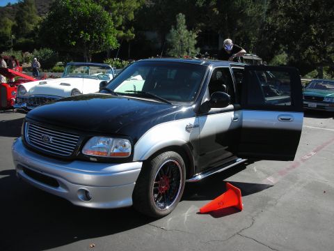1998 Ford Crown Victoria - black-and-silver custom Ford F-150 pickup sits with its door open in a car-show parking lot.