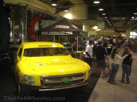 1990 Ford Bronco - yellow Chevrolet short-course off-road race truck on display under a CORR Championship Off Road Racing banner at an expo.
