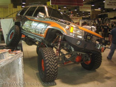 1990 Ford Bronco - heavily lifted SUV built as a rock crawler with long-travel suspension, orange beadlock wheels and Toyo Tires graphics on the expo floor.