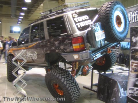 1990 Ford Bronco - Rear three-quarter view of a lifted off-road SUV with a roof-mounted spare tire, coilover suspension and Toyo Tires livery at an expo.