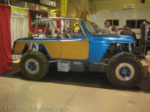 1990 Ford Bronco - Side profile of a blue custom open-top 4x4 with wood-grain side panels, roll cage and large tires on beadlock wheels at an expo booth.
