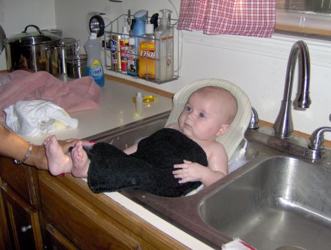 1978 Ford Bronco - A baby is being bathed in a kitchen sink, with a person's hand holding their feet.