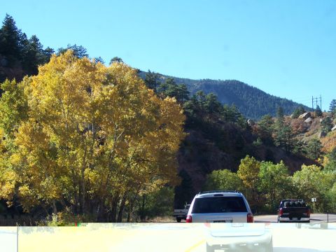 1972 Ford Ranchero - Two vehicles drive along a road bordered by trees in autumn colors, with mountains in the background under a clear blue sky.
