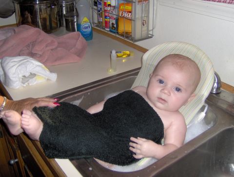 1978 Ford Bronco - A baby is taking a bath in a kitchen sink, wrapped in a black towel.