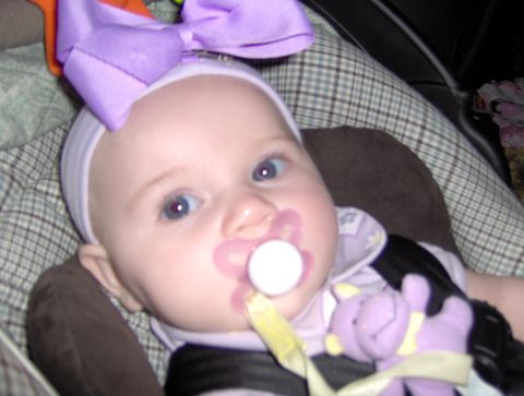 1978 Ford Bronco - A baby wearing a large purple bow and a pacifier is secured in a car seat.