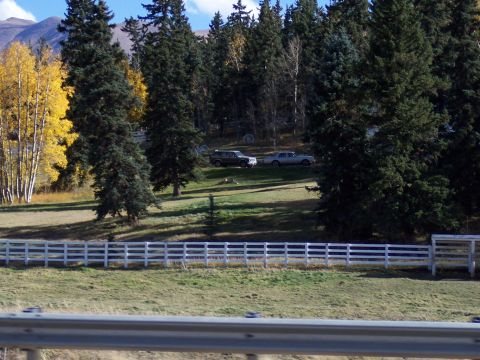 1972 Ford Ranchero - A dark SUV and a light-colored sedan are parked on a hill, surrounded by trees and mountains under a blue sky.