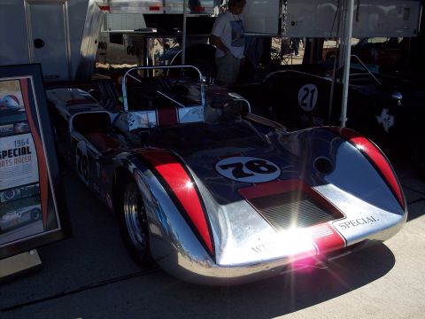 1971 Ford Mustang - A vintage race car with a polished metal body and red accents is displayed under a tent.