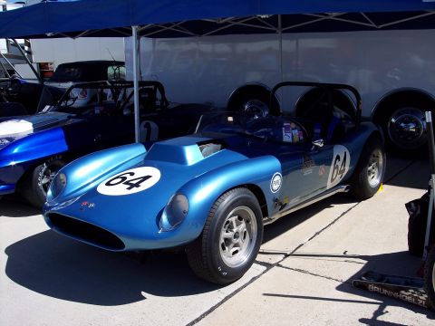 1971 Ford Mustang - A blue race car with the number 64 is parked next to another vehicle under a blue canopy.