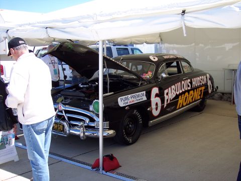 1971 Ford Mustang - A black 1950s Hudson Hornet race car, number 6, is displayed under a tent with its hood open.