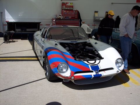 1971 Ford Mustang - A race car with its hood open, displaying the engine, is parked in a garage bay.