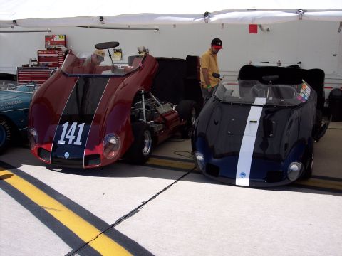 1971 Ford Mustang - Two open-cockpit race cars are parked side-by-side in a garage area.