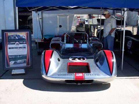 1971 Ford Mustang - 1964 Webster Special sports racer displayed under a blue canopy with a framed poster nearby.