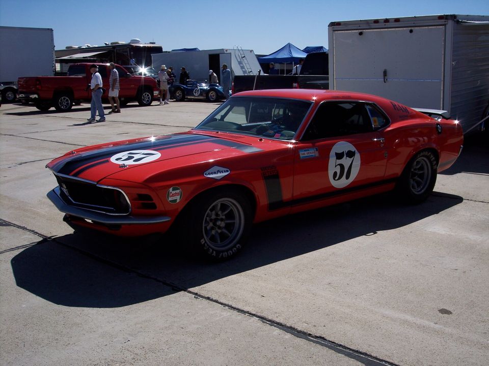 Red 1969 Mustang race car with black stripes and number 57 on hood and door. Goodyear tires visible
