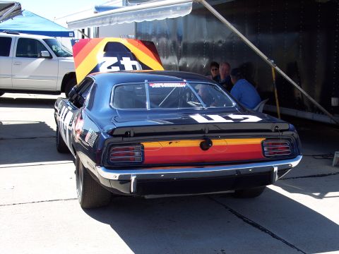 1971 Ford Mustang - A dark blue 1970 Plymouth Barracuda race car is parked with its hood up, next to a white SUV and a trailer.