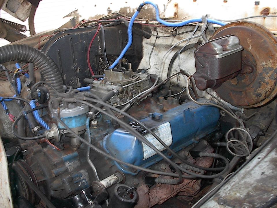 Blue V8 engine with carburetor and blue plug wires in a rusty engine bay