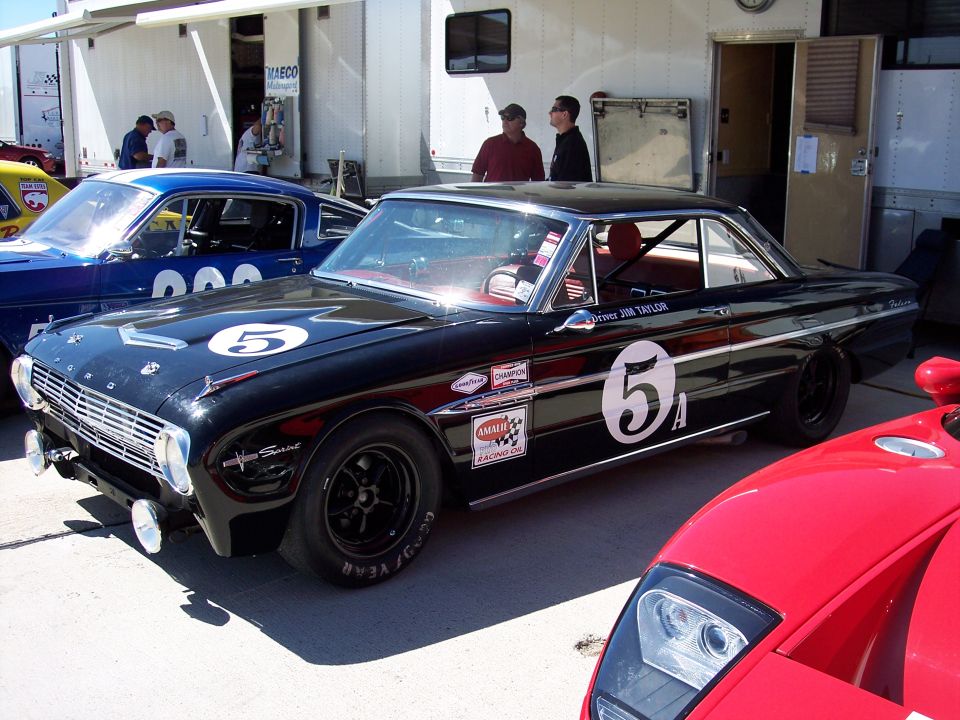 Black 1963 Ford Falcon Sprint race car with number 5 on hood and door, parked next to a blue Mustang and a red sports car