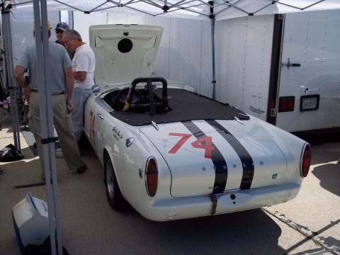 1971 Ford Mustang - A white Sunbeam convertible with racing stripes and the number 74 is parked under a canopy.