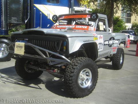 1990 Ford Bronco - silver Rubicon-bodied Jeepspeed race truck numbered 3701 shows its tubular front bumper and beadlock wheels on outdoor pavement.