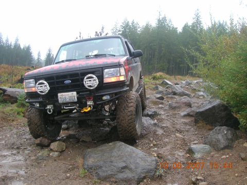 1996 Ford Bronco - A black 1996 Ford Bronco navigates a challenging rocky trail, equipped with Hella lights and an aftermarket bumper.