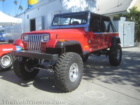 1990 Ford Bronco - red lifted Jeep Wrangler with the top removed sits on large mud tires and a suspension lift at an outdoor display.