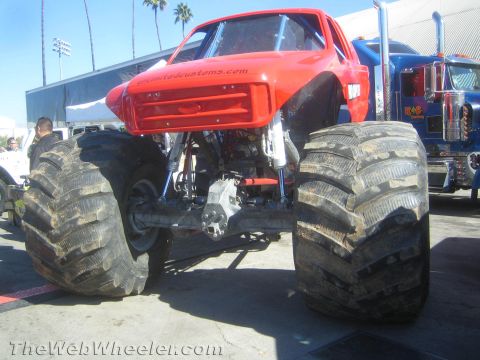 1990 Ford Bronco - red-bodied monster truck rests on enormous tractor-style tires showing its bare tube chassis at an outdoor display.