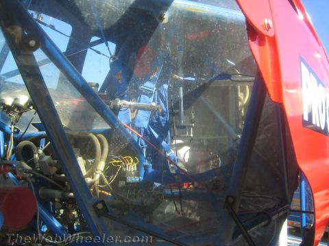 1990 Ford Bronco - close-up looks through a clear window into the wiring, plumbing and blue tubular interior of a race vehicle.