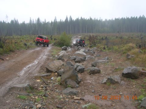 1996 Ford Bronco - Two SUVs drive through a challenging, rocky, and muddy off-road course on a cloudy day.