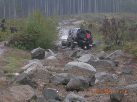 1996 Ford Bronco - A Ford Bronco drives through a challenging, rocky off-road course on a cloudy day.