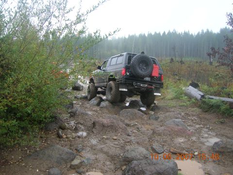 1996 Ford Bronco - A 1996 Ford Bronco tackles a challenging off-road course with large rocks and mud.