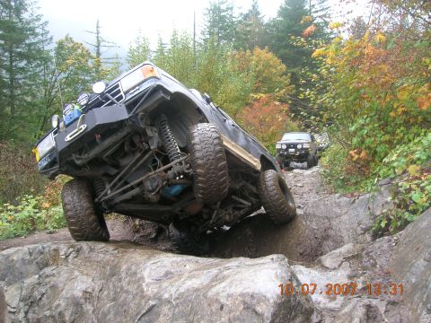 1996 Ford Bronco - Two off-road vehicles navigate a challenging rocky trail with autumn foliage in the background.