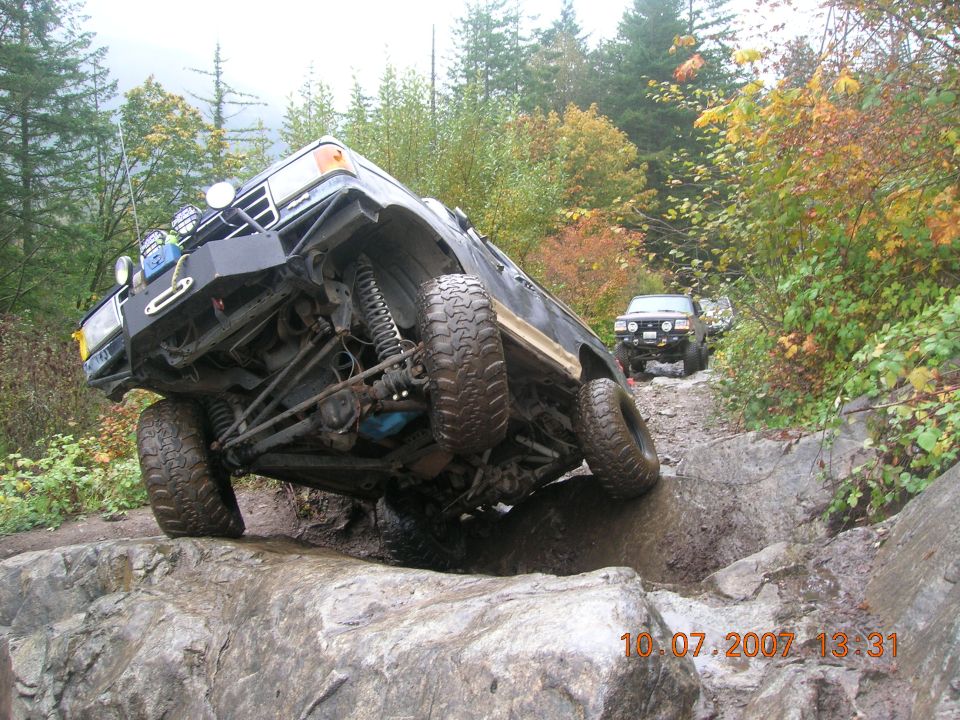 off-road vehicle climbing over rocks on a trail, another vehicle behind it