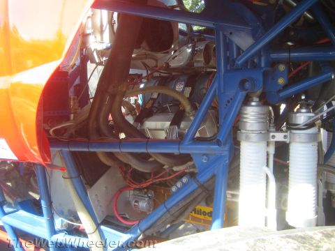 1990 Ford Bronco - close-up of an engine compartment shows blue tubular framing, exhaust headers and twin white coilover shocks.