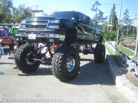 1990 Ford Bronco - black Chevrolet crew-cab pickup on a very tall suspension lift and large mud tires sits on display in an outdoor park setting.