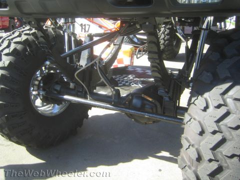 1990 Ford Bronco - close-up shows a chrome solid axle, leaf springs and driveshaft between large off-road tires beneath a lifted vehicle.